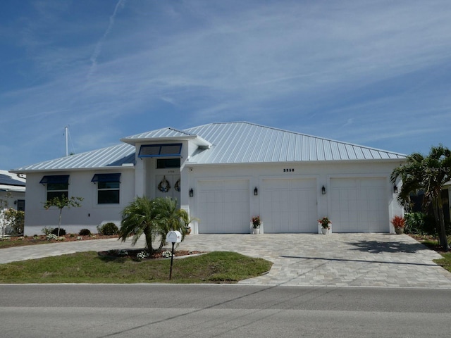 single story home featuring a standing seam roof, metal roof, a garage, stucco siding, and decorative driveway