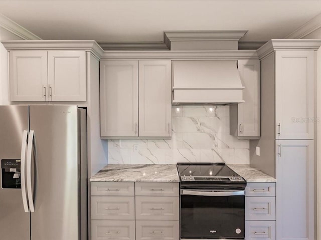 kitchen featuring black / electric stove, stainless steel fridge, tasteful backsplash, light stone counters, and custom range hood