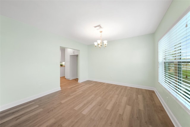 empty room with light hardwood / wood-style floors and an inviting chandelier