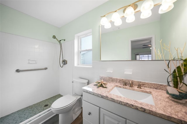 bathroom with vanity, ceiling fan, toilet, tiled shower, and tile walls