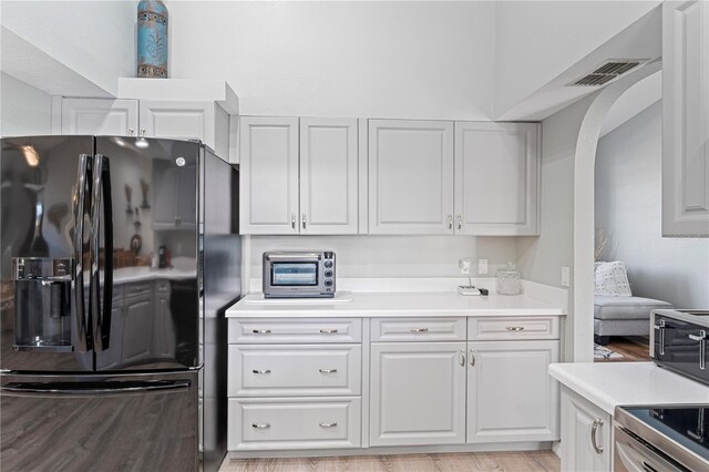 kitchen featuring white cabinets, range, black refrigerator with ice dispenser, and light hardwood / wood-style flooring