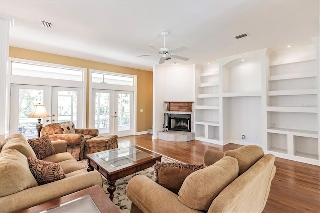 living room featuring built in shelves, ceiling fan, dark wood-type flooring, and french doors