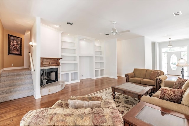 living room featuring built in shelves, light hardwood / wood-style floors, ceiling fan, and a tiled fireplace