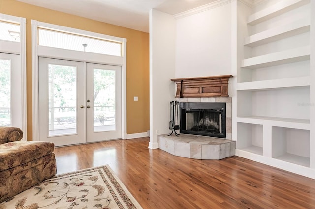 living room featuring built in shelves, a tiled fireplace, french doors, and wood-type flooring