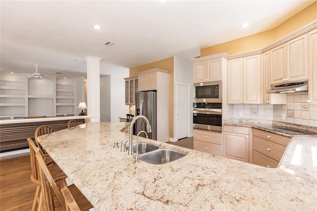 kitchen with a breakfast bar, sink, decorative backsplash, light stone counters, and stainless steel appliances