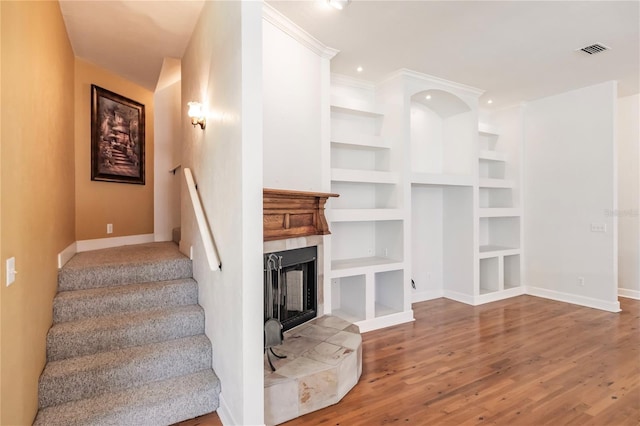 unfurnished living room featuring a tile fireplace, built in shelves, crown molding, and hardwood / wood-style floors