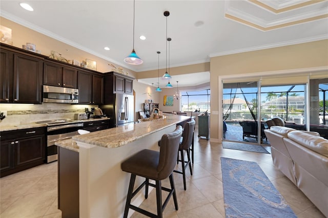 kitchen with stainless steel appliances, decorative light fixtures, a kitchen bar, a center island with sink, and ornamental molding