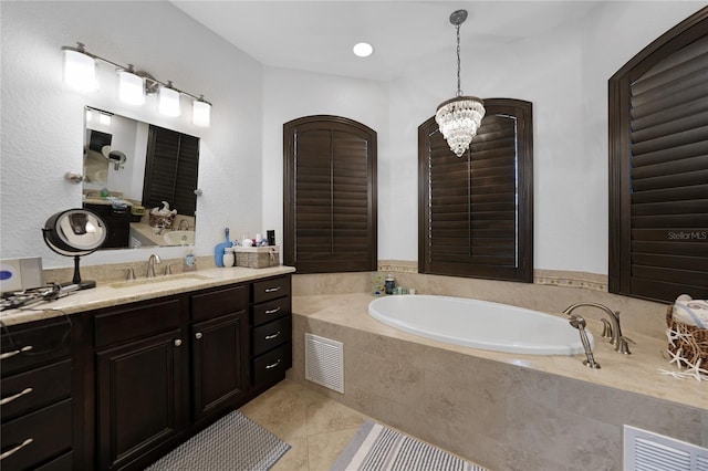 bathroom with tile patterned flooring, vanity, an inviting chandelier, and tiled tub