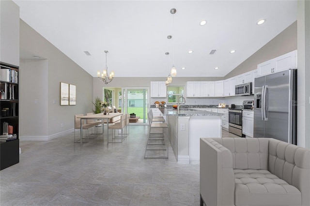 kitchen featuring pendant lighting, a center island, appliances with stainless steel finishes, light stone counters, and white cabinetry