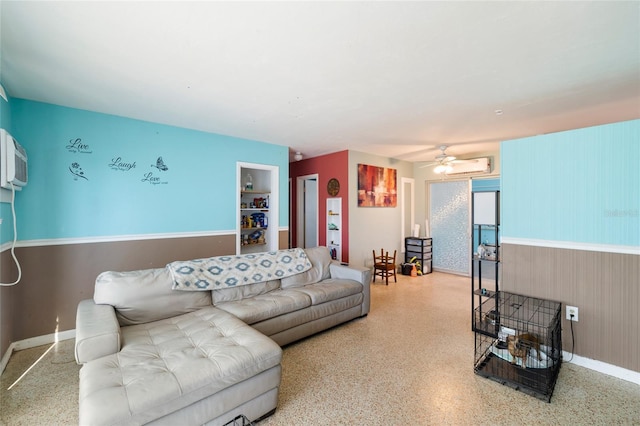 living room with built in features, a wall unit AC, and ceiling fan