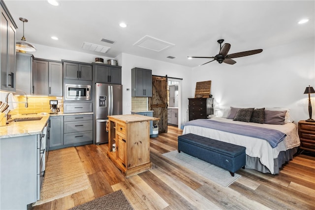 bedroom featuring ceiling fan, sink, a barn door, stainless steel fridge, and light hardwood / wood-style floors