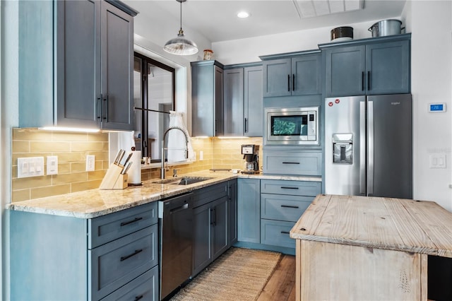 kitchen featuring hanging light fixtures, sink, light hardwood / wood-style flooring, appliances with stainless steel finishes, and tasteful backsplash