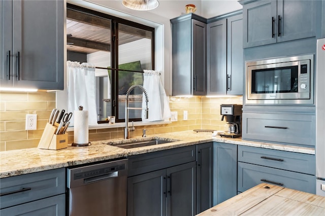 kitchen featuring decorative backsplash, sink, light stone countertops, and appliances with stainless steel finishes