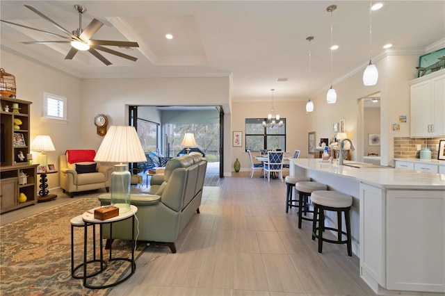 living room with plenty of natural light, ornamental molding, ceiling fan with notable chandelier, and sink