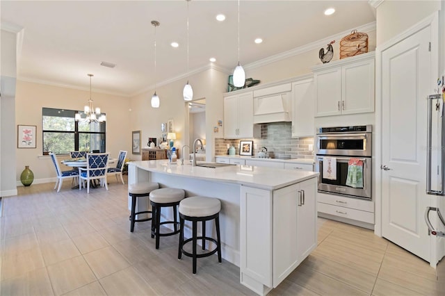 kitchen featuring pendant lighting, a center island with sink, stainless steel double oven, light tile patterned floors, and white cabinetry