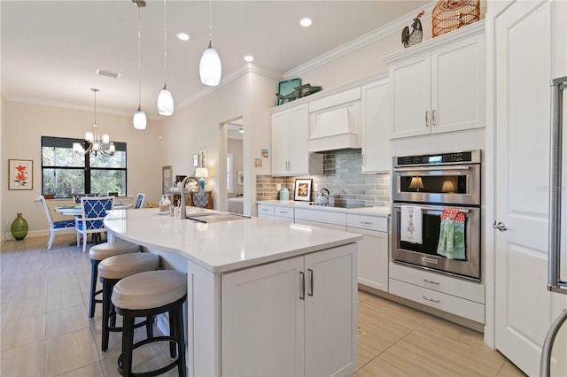 kitchen with pendant lighting, an island with sink, stainless steel double oven, and custom range hood