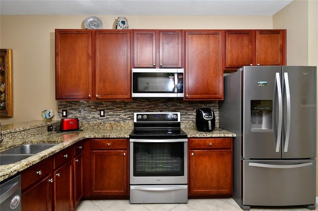 kitchen featuring light stone countertops, sink, tasteful backsplash, light tile patterned flooring, and appliances with stainless steel finishes