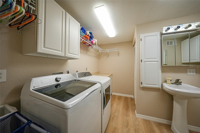 laundry area with cabinets, sink, washer and dryer, light wood-type flooring, and a textured ceiling