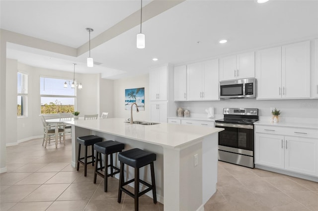 kitchen featuring a kitchen island with sink, sink, appliances with stainless steel finishes, decorative light fixtures, and white cabinetry