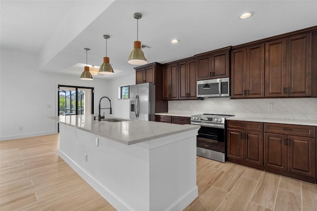 kitchen featuring a kitchen island with sink, sink, decorative backsplash, appliances with stainless steel finishes, and decorative light fixtures