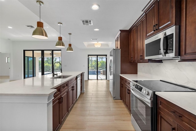 kitchen with tasteful backsplash, stainless steel appliances, sink, pendant lighting, and light hardwood / wood-style flooring