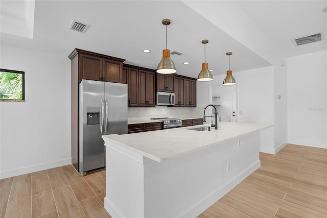 kitchen with appliances with stainless steel finishes, dark brown cabinetry, sink, pendant lighting, and an island with sink