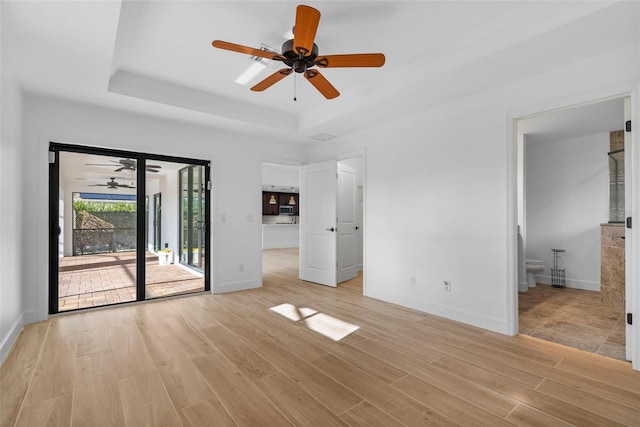 unfurnished bedroom with access to outside, a raised ceiling, ceiling fan, light hardwood / wood-style flooring, and connected bathroom