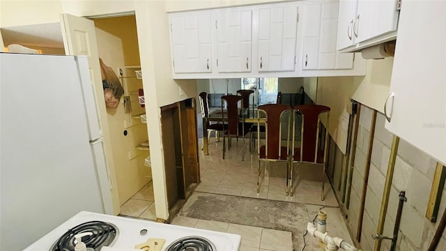 kitchen featuring range, white cabinets, light tile patterned floors, and white refrigerator