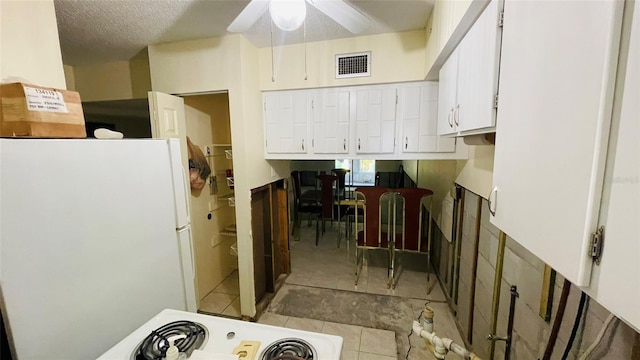 kitchen featuring stove, a textured ceiling, ceiling fan, white fridge, and white cabinetry