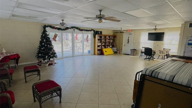 interior space with a paneled ceiling, ceiling fan, light tile patterned floors, and access to exterior