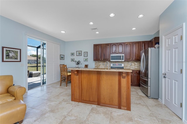 kitchen featuring decorative backsplash, range, an island with sink, and stainless steel refrigerator