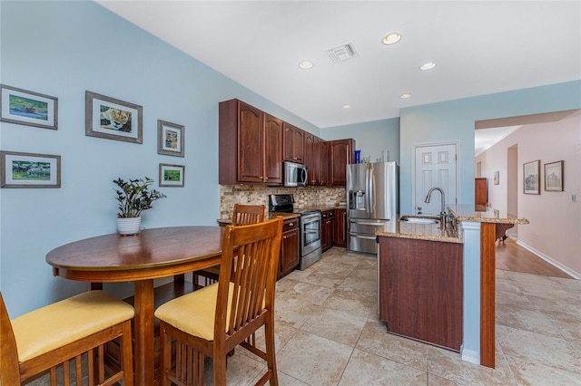 kitchen with tasteful backsplash, light stone counters, sink, and appliances with stainless steel finishes