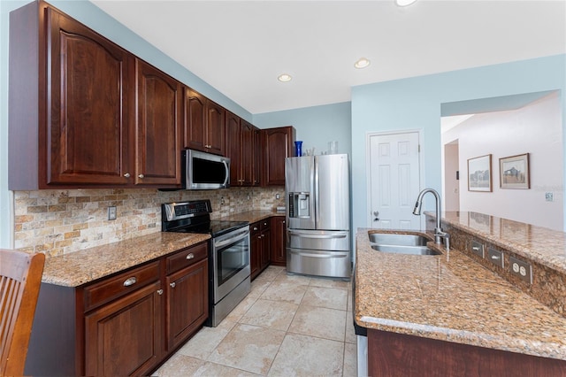 kitchen with sink, tasteful backsplash, light stone counters, dark brown cabinets, and appliances with stainless steel finishes