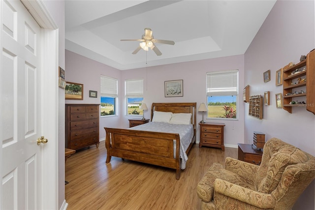 bedroom with ceiling fan, a raised ceiling, and light hardwood / wood-style flooring