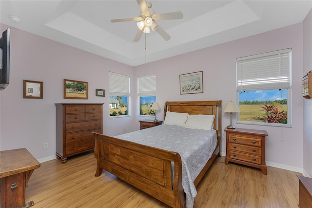 bedroom with ceiling fan, a raised ceiling, and light wood-type flooring