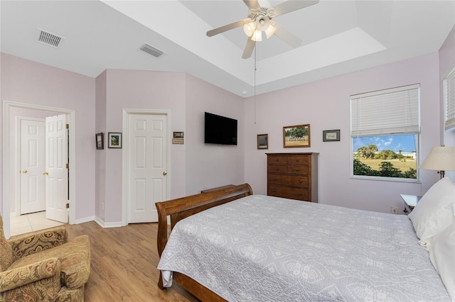 bedroom featuring light wood-type flooring, a tray ceiling, and ceiling fan