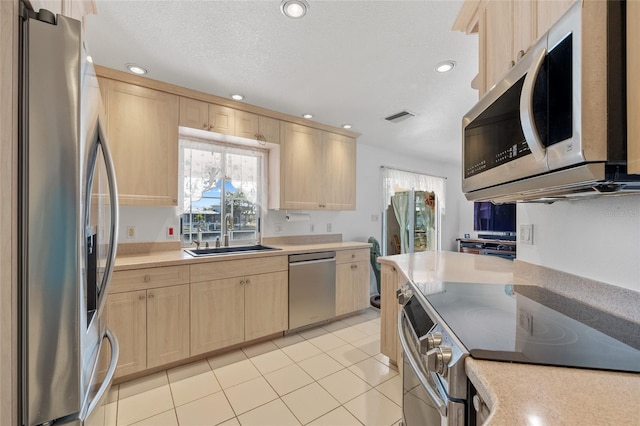 kitchen with stainless steel appliances, light tile patterned floors, a textured ceiling, light brown cabinets, and sink