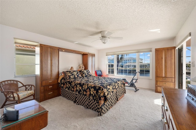 bedroom with ceiling fan, light colored carpet, multiple windows, and a textured ceiling