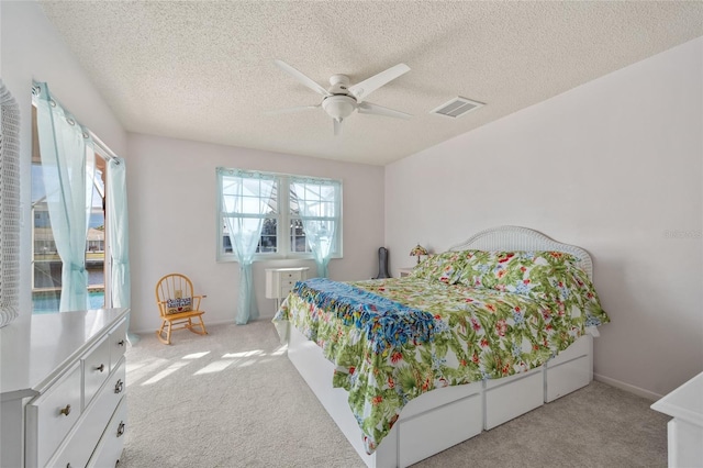 bedroom with ceiling fan, light carpet, and a textured ceiling