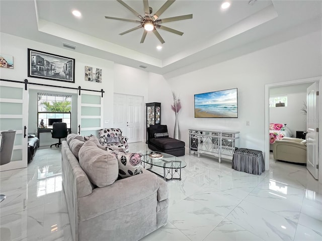 living room with a tray ceiling, a barn door, ceiling fan, and a high ceiling