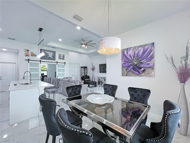 dining room featuring ceiling fan with notable chandelier, a barn door, a tray ceiling, and sink