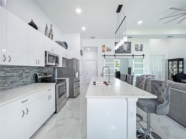 kitchen featuring sink, stainless steel appliances, a barn door, pendant lighting, and a breakfast bar