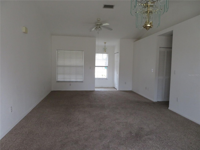 carpeted spare room featuring ceiling fan with notable chandelier