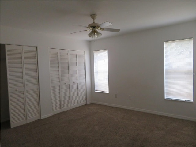 unfurnished bedroom featuring dark colored carpet, two closets, and ceiling fan