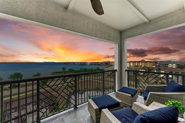 balcony at dusk featuring ceiling fan and a water view