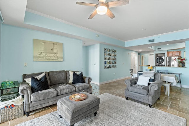 living room with a tray ceiling, ceiling fan, stacked washer and clothes dryer, and ornamental molding