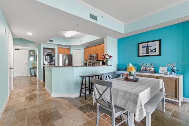 dining area with crown molding and stacked washer and clothes dryer