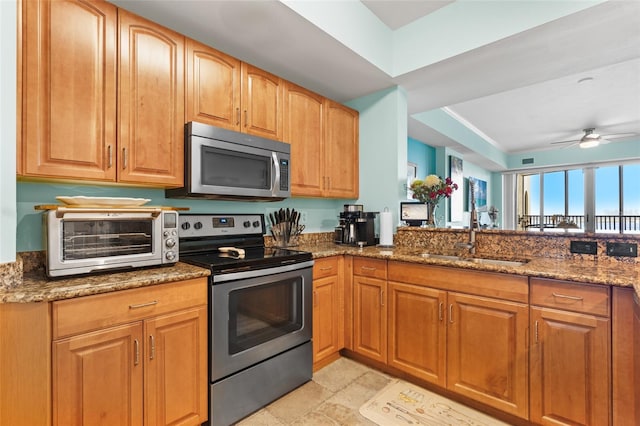 kitchen with stainless steel appliances, ceiling fan, dark stone countertops, and sink