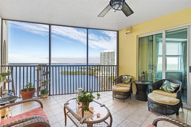 sunroom with ceiling fan and a water view