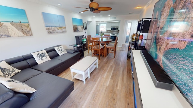 living room with ceiling fan, ornamental molding, and light wood-type flooring